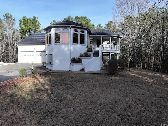 view of front of property featuring covered porch, solar panels, a garage, concrete driveway, and stairway