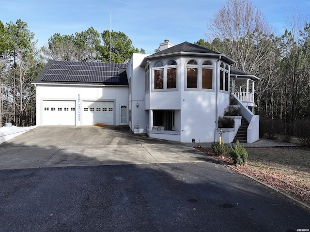 view of front of property featuring concrete driveway, a chimney, stairway, an attached garage, and roof mounted solar panels