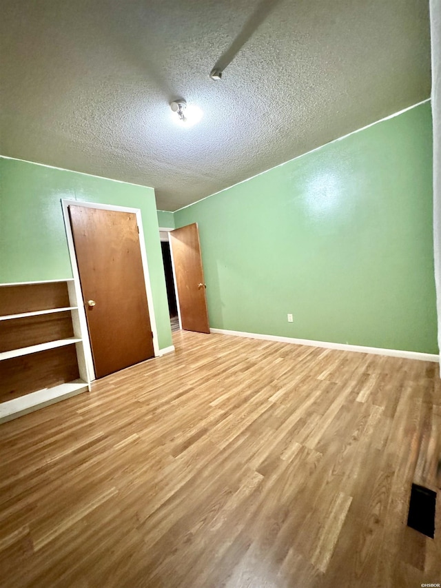 unfurnished bedroom with a closet, a textured ceiling, baseboards, and wood finished floors