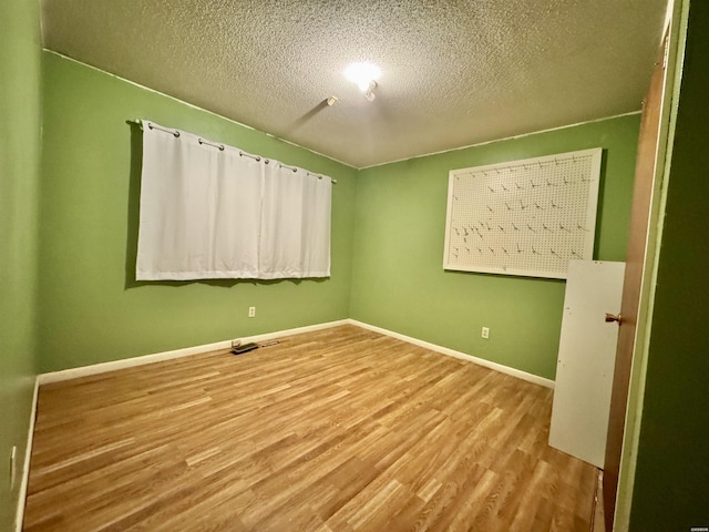 empty room featuring a textured ceiling, light wood-type flooring, and baseboards