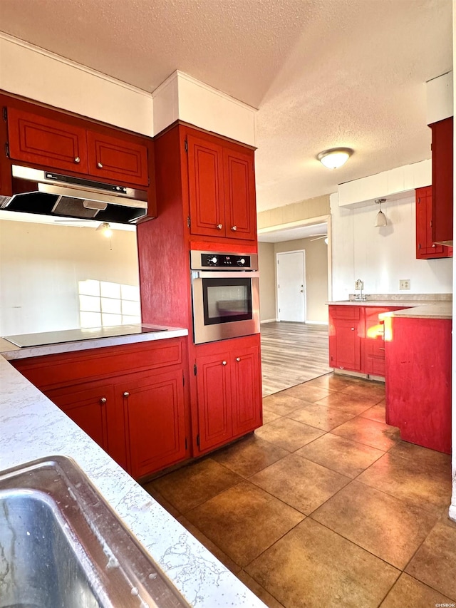 kitchen with oven, black electric stovetop, light countertops, under cabinet range hood, and dark tile patterned floors