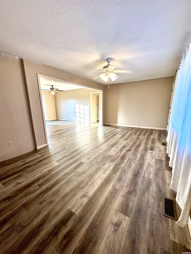 empty room featuring baseboards, visible vents, a ceiling fan, dark wood-style flooring, and a textured ceiling