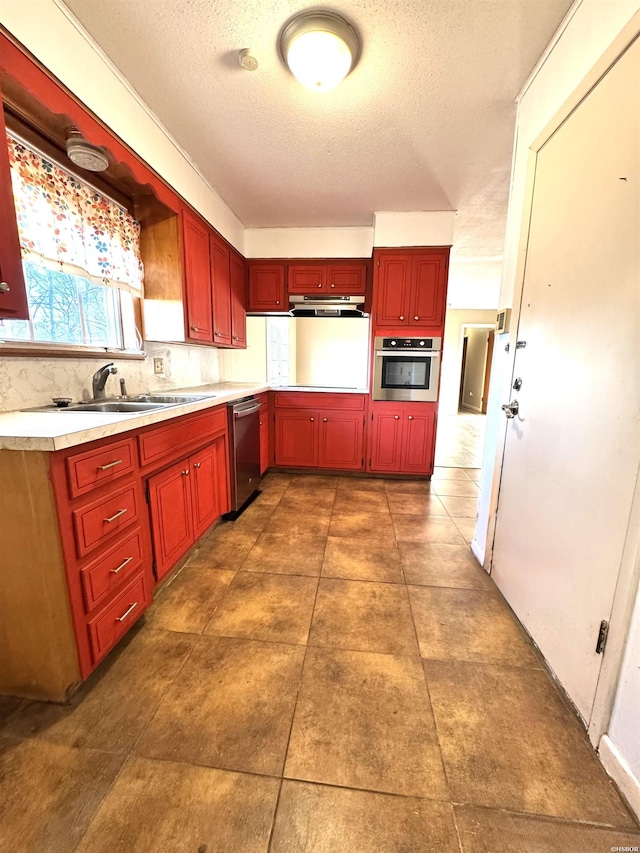 kitchen with stainless steel appliances, tasteful backsplash, light countertops, a sink, and under cabinet range hood