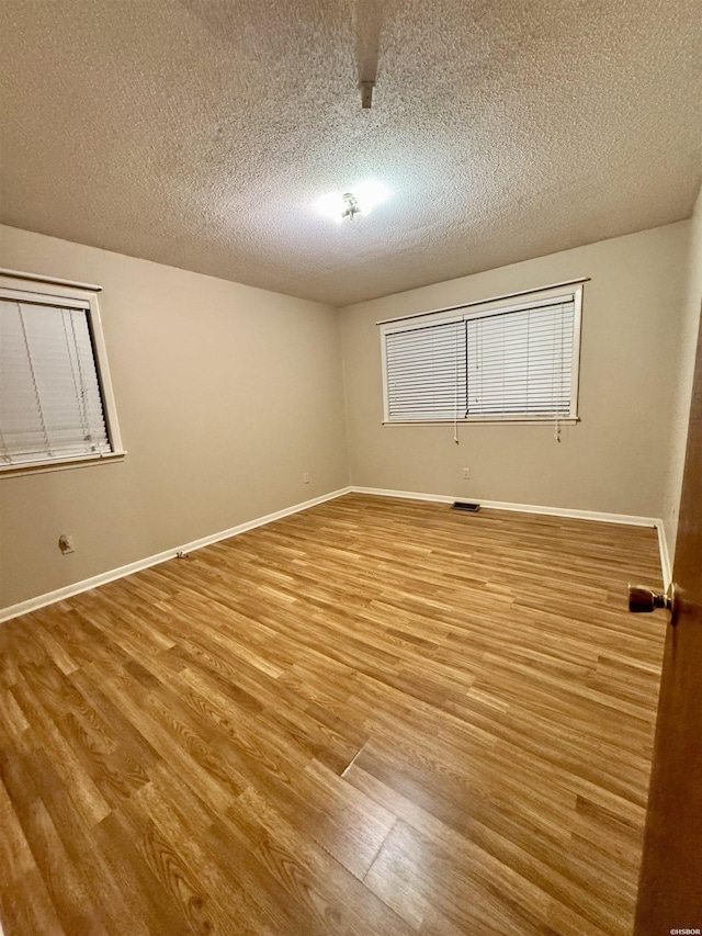 spare room with a textured ceiling, wood finished floors, visible vents, and baseboards