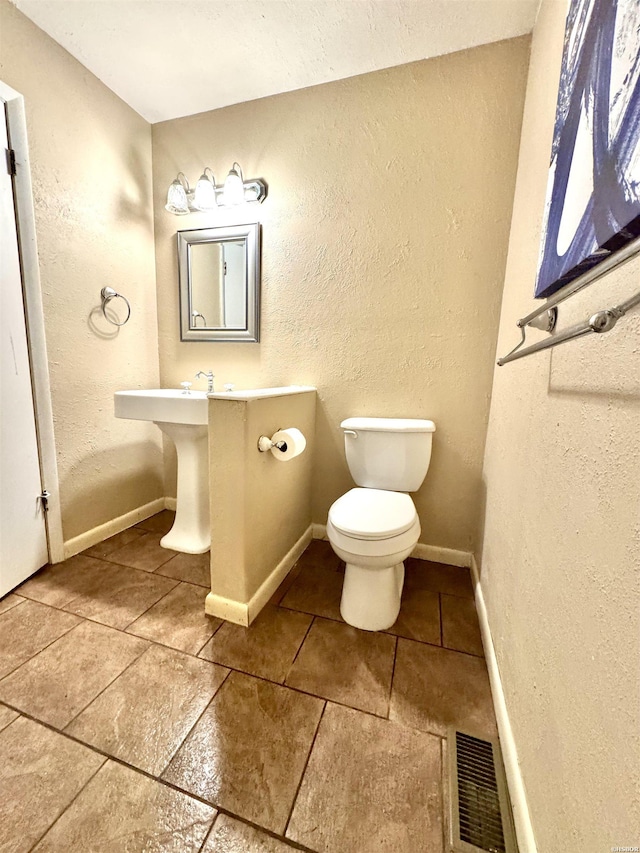 half bathroom featuring baseboards, visible vents, a textured wall, and toilet