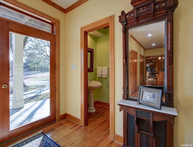 interior space with light wood-type flooring, visible vents, crown molding, and baseboards