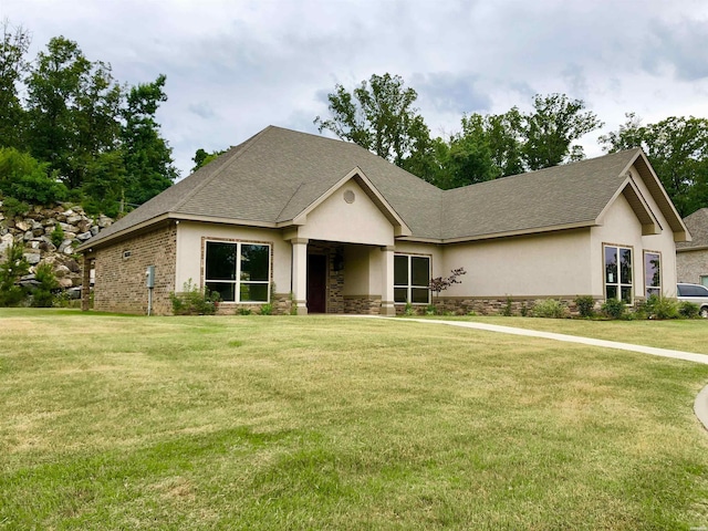 view of front of property with stone siding, roof with shingles, a front yard, and stucco siding