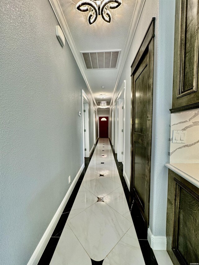 hallway featuring a textured ceiling, a textured wall, visible vents, baseboards, and ornamental molding