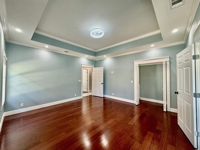 unfurnished bedroom with dark wood-type flooring, visible vents, baseboards, ornamental molding, and a raised ceiling