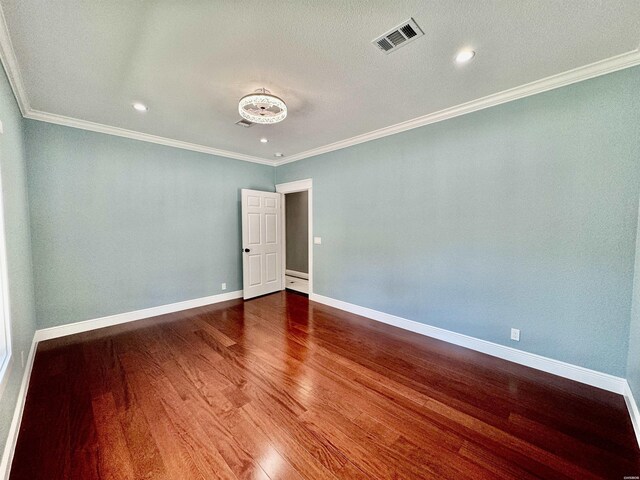 unfurnished room featuring baseboards, visible vents, wood finished floors, and ornamental molding