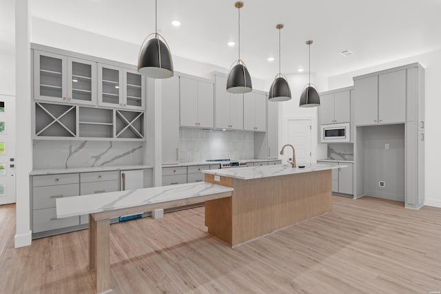 kitchen with hanging light fixtures, an island with sink, light stone countertops, and built in microwave