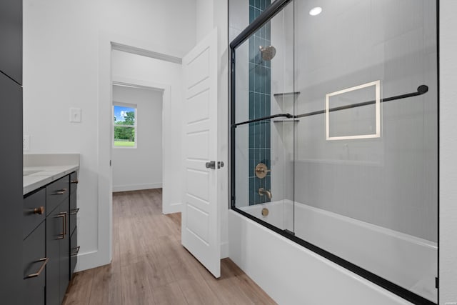 full bath with baseboards, bath / shower combo with glass door, wood finished floors, and vanity