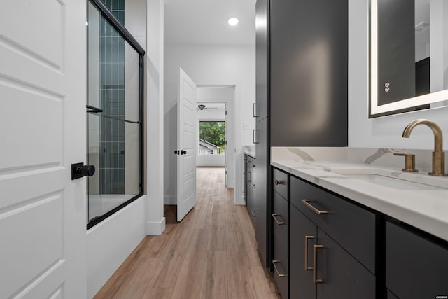 full bath with recessed lighting, combined bath / shower with glass door, vanity, wood finished floors, and baseboards