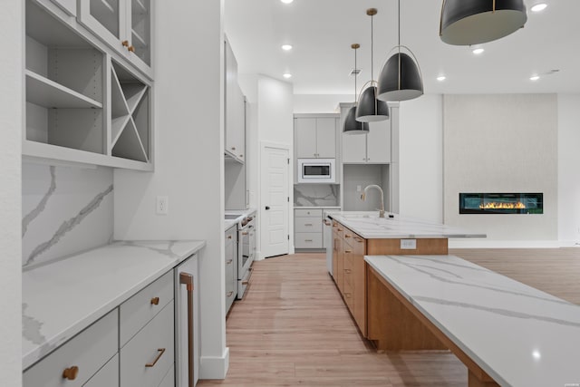 kitchen with white cabinets, hanging light fixtures, light stone countertops, a kitchen island with sink, and built in microwave