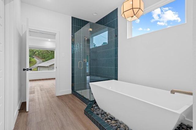 full bathroom with wood finished floors, a stall shower, a freestanding tub, and baseboards