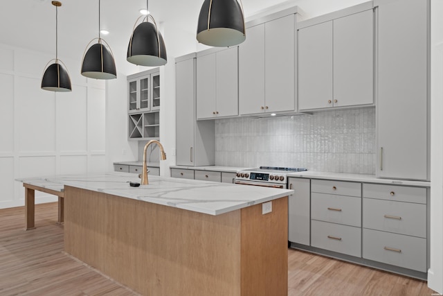 kitchen featuring tasteful backsplash, high end range oven, a kitchen island with sink, and decorative light fixtures