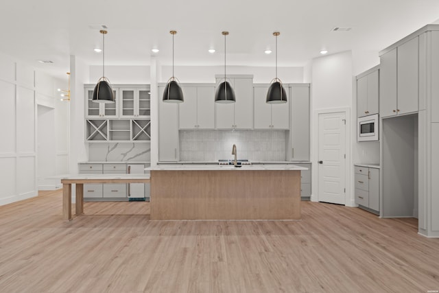 kitchen with a center island with sink, white microwave, hanging light fixtures, light countertops, and light wood-style floors