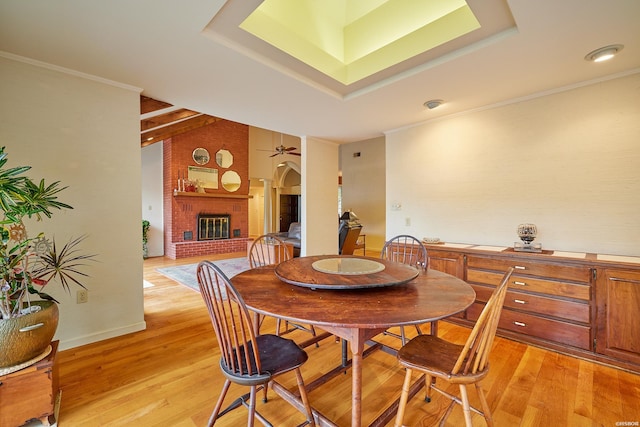 dining area featuring a tray ceiling, light wood finished floors, a fireplace, and crown molding