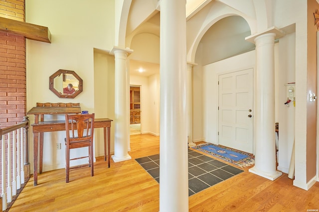 foyer with arched walkways, decorative columns, a high ceiling, and wood finished floors