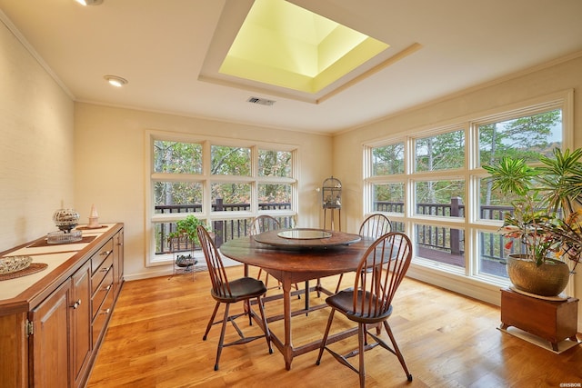 dining area with a skylight, a tray ceiling, visible vents, light wood-style floors, and ornamental molding