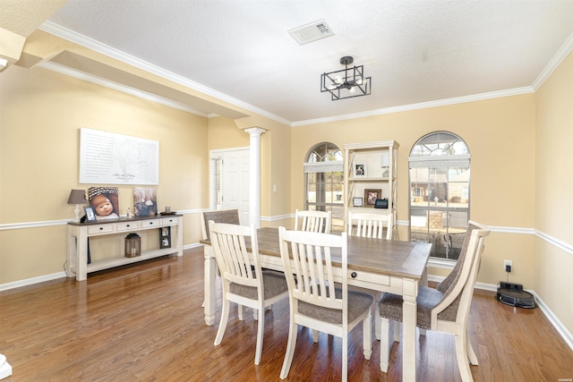 dining area with decorative columns, baseboards, visible vents, wood finished floors, and crown molding