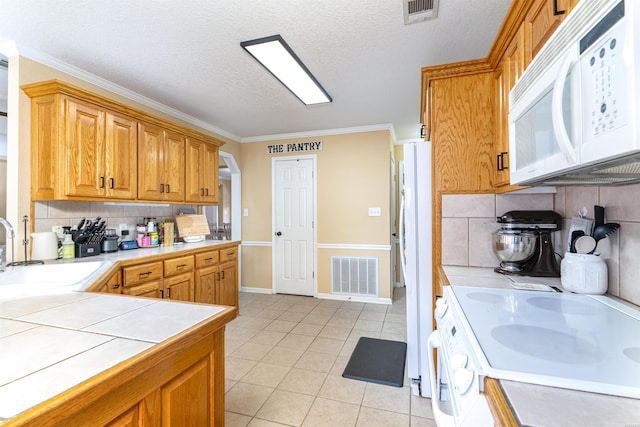 kitchen featuring light tile patterned flooring, white appliances, a sink, visible vents, and tile counters