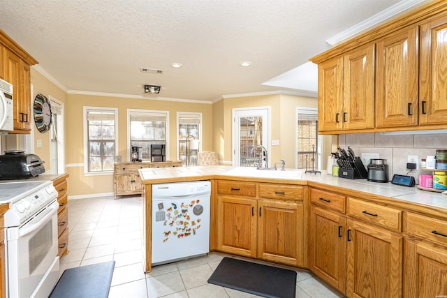 kitchen featuring a peninsula, white appliances, ornamental molding, and a sink