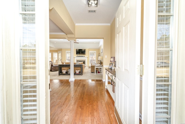 foyer entrance featuring a fireplace, visible vents, ornamental molding, light wood finished floors, and ornate columns