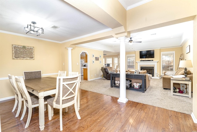 dining area with decorative columns, visible vents, ceiling fan, wood finished floors, and a fireplace