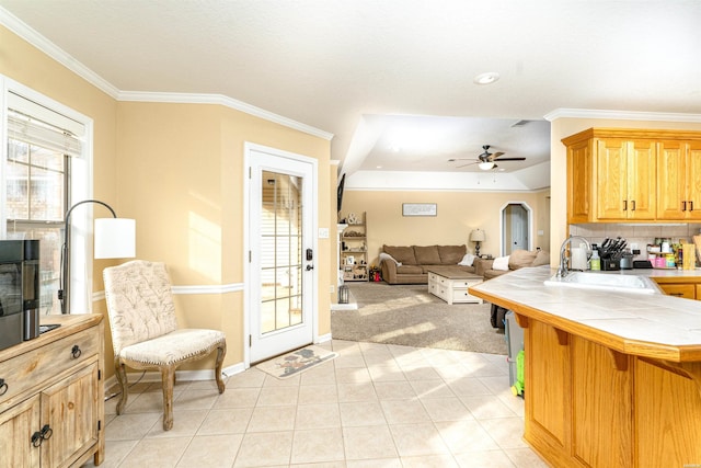 kitchen with arched walkways, tile counters, ornamental molding, open floor plan, and a sink