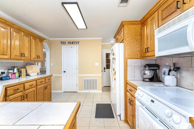 kitchen with white appliances, light tile patterned floors, visible vents, and tile counters