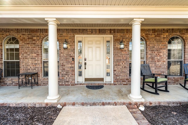 entrance to property featuring a porch and brick siding