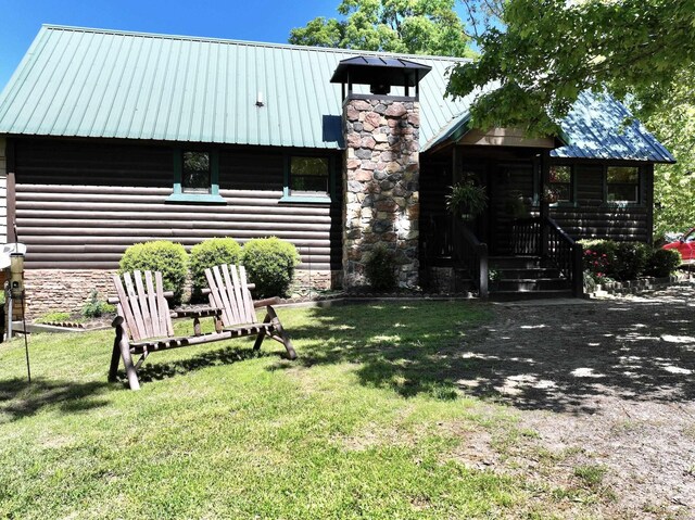 exterior space with faux log siding, a chimney, metal roof, and a lawn