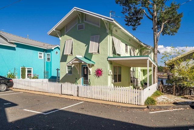 view of front facade featuring a fenced front yard, uncovered parking, metal roof, and stucco siding