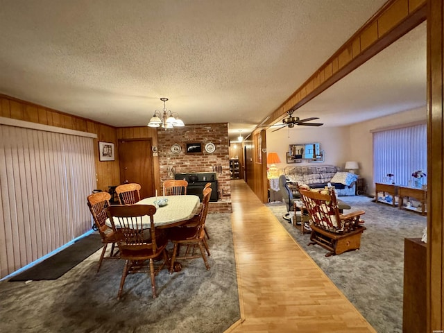 carpeted dining area with a textured ceiling, wood walls, and ceiling fan with notable chandelier