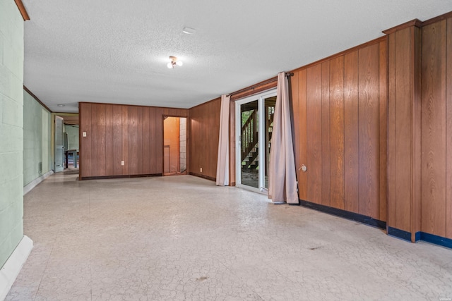 spare room with a textured ceiling, baseboards, and wooden walls