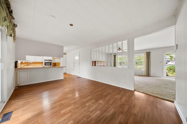 unfurnished living room with light wood-type flooring, visible vents, and a ceiling fan