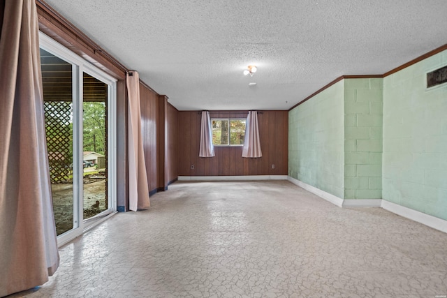 empty room with concrete block wall, a textured ceiling, and baseboards