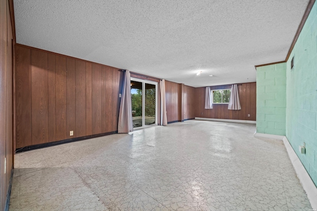 empty room featuring a textured ceiling, wood walls, baseboards, light floors, and concrete block wall