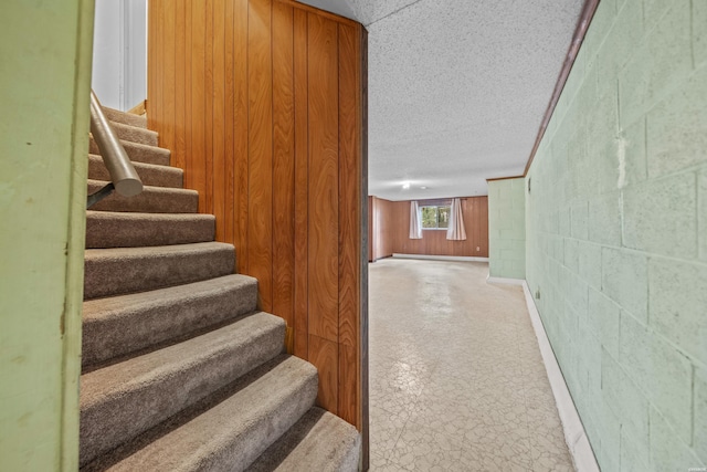 stairway with a textured ceiling, concrete block wall, and tile patterned floors