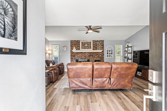 living room with light wood-style floors, vaulted ceiling, a fireplace, and ceiling fan