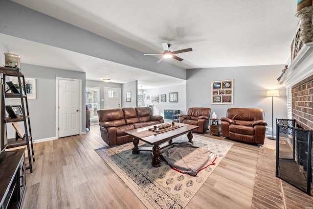 living area featuring vaulted ceiling, light wood-type flooring, a brick fireplace, and baseboards