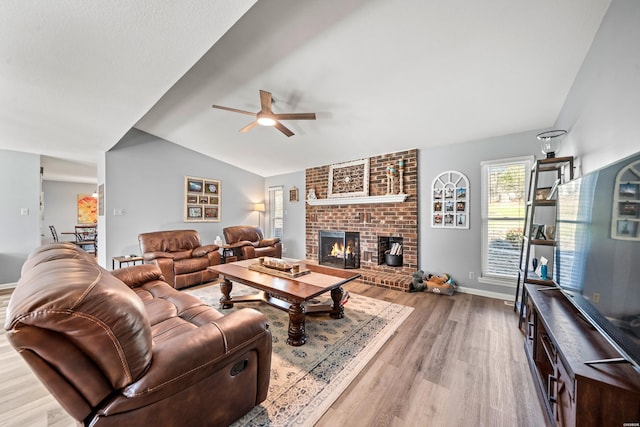 living area featuring a fireplace, a ceiling fan, baseboards, vaulted ceiling, and light wood-style floors