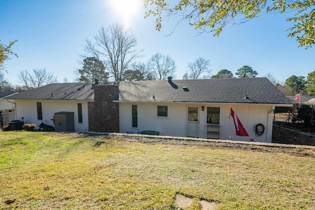 back of property featuring a shingled roof, a chimney, and a lawn