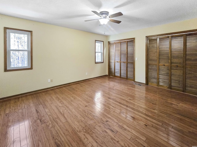 unfurnished bedroom with ceiling fan, visible vents, baseboards, light wood finished floors, and two closets