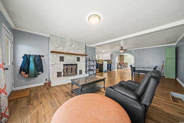 living room featuring ornamental molding, a stone fireplace, a textured ceiling, and wood finished floors