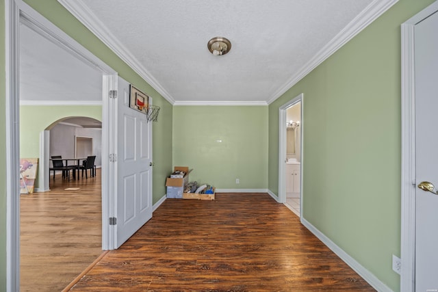 corridor featuring arched walkways, baseboards, wood finished floors, and crown molding