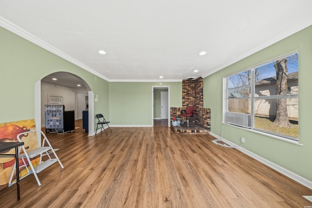 living area with ornamental molding, arched walkways, baseboards, and wood finished floors