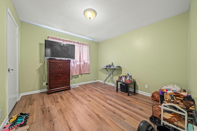 recreation room featuring a textured ceiling, baseboards, and wood finished floors