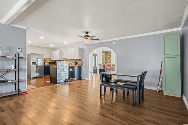 dining room with dark wood-style floors, arched walkways, ornamental molding, and a ceiling fan